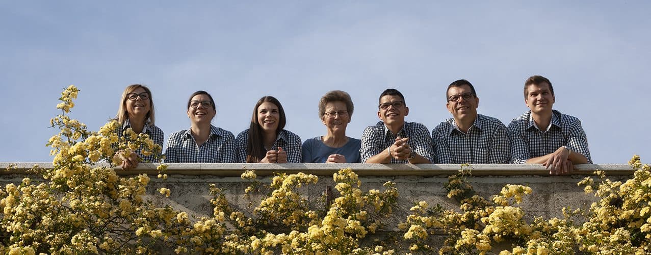 The Pucer family behind a stone wall with roses in front of Hiša Padnjec